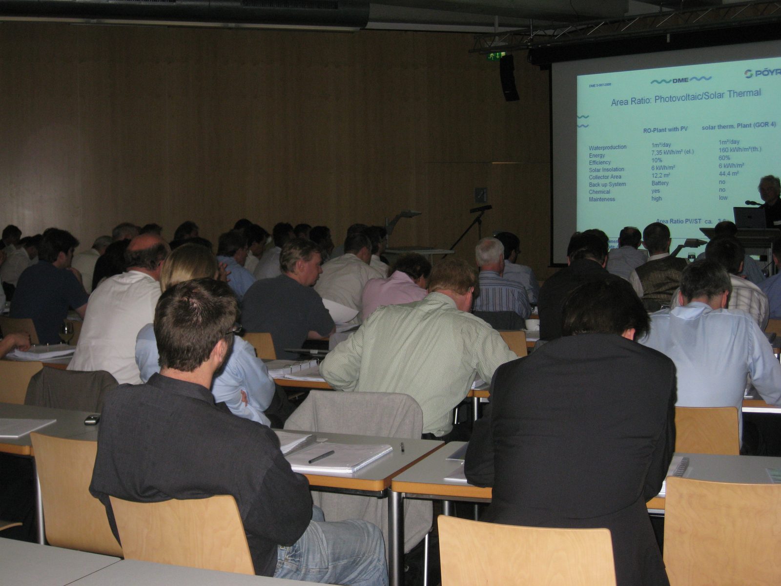 Fully occupied lecture hall during a DME seminar, participants seen from behind, presentation slide on the screen
